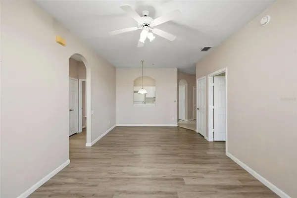 an empty room with wooden floor chandelier fan and windows