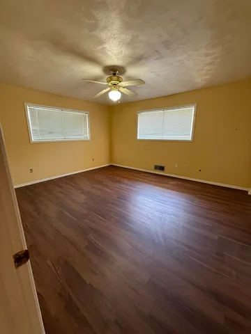 an empty room with wooden floor chandelier fan and windows