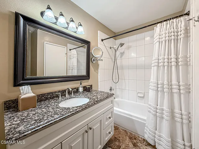 a bathroom with a granite countertop sink a mirror a vanity and a bathtub