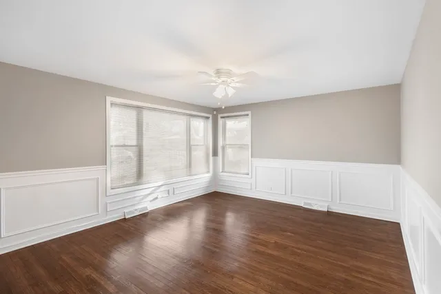 an empty room with wooden floor and windows with curtains