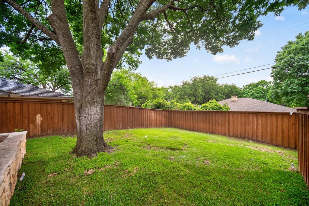 9660 Timberleaf Drive Dallas, TX 75243 - Photo 40 of 40 Expansive grassy backyard featuring a mature shade tree, a new wood privacy fence, and a stone retaining wall
