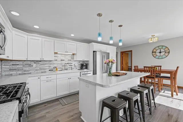 a kitchen with stainless steel appliances granite countertop a stove top oven a refrigerator a dining table and chairs with wooden floor