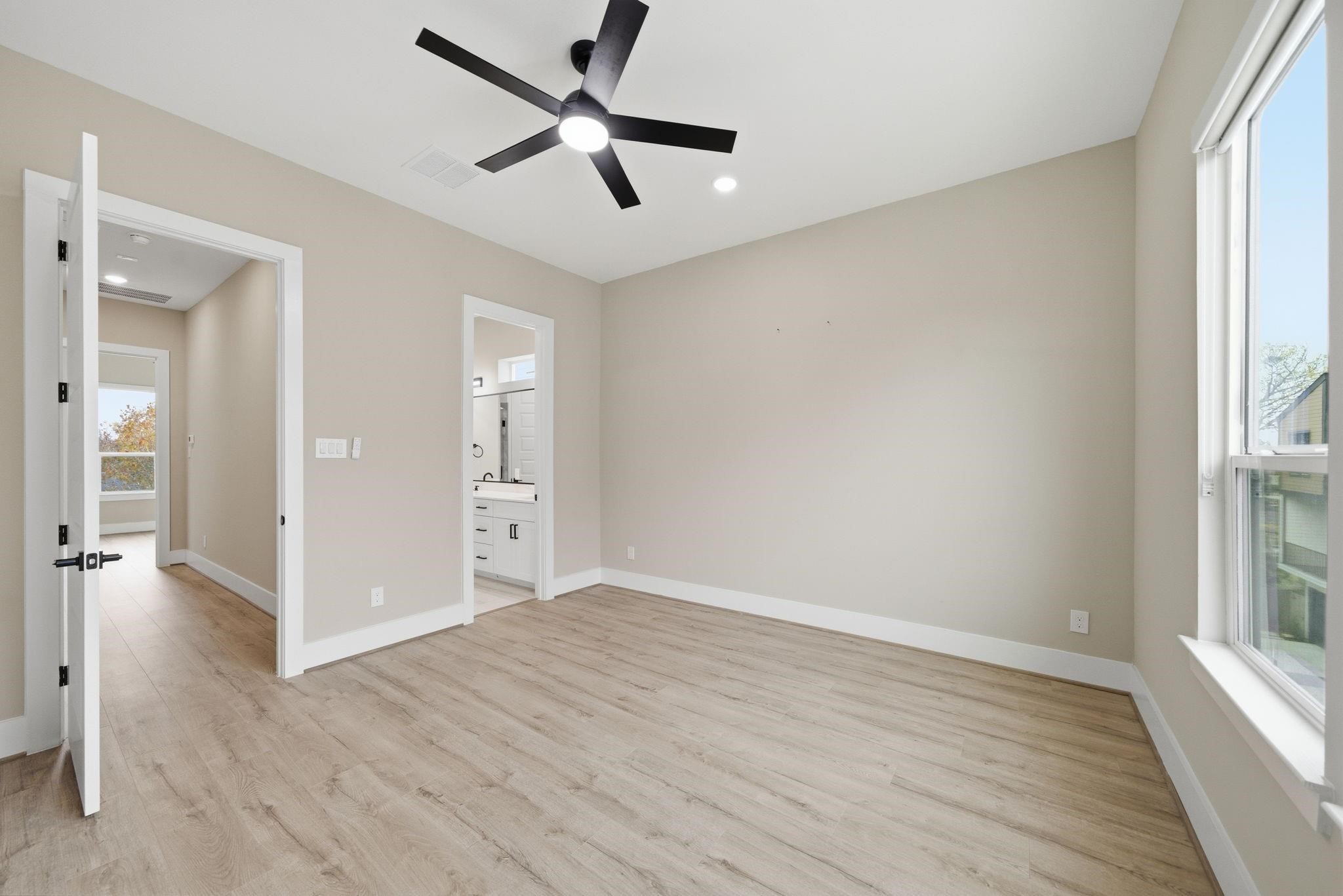 4013 Griggs Road, Unit F Houston, TX 77021 - Photo 15 of 35 Bright and spacious bedroom featuring sleek hardwood floors, a modern ceiling fan, and ample natural light from large windows, with convenient access to a stylish en-suite bathroom.