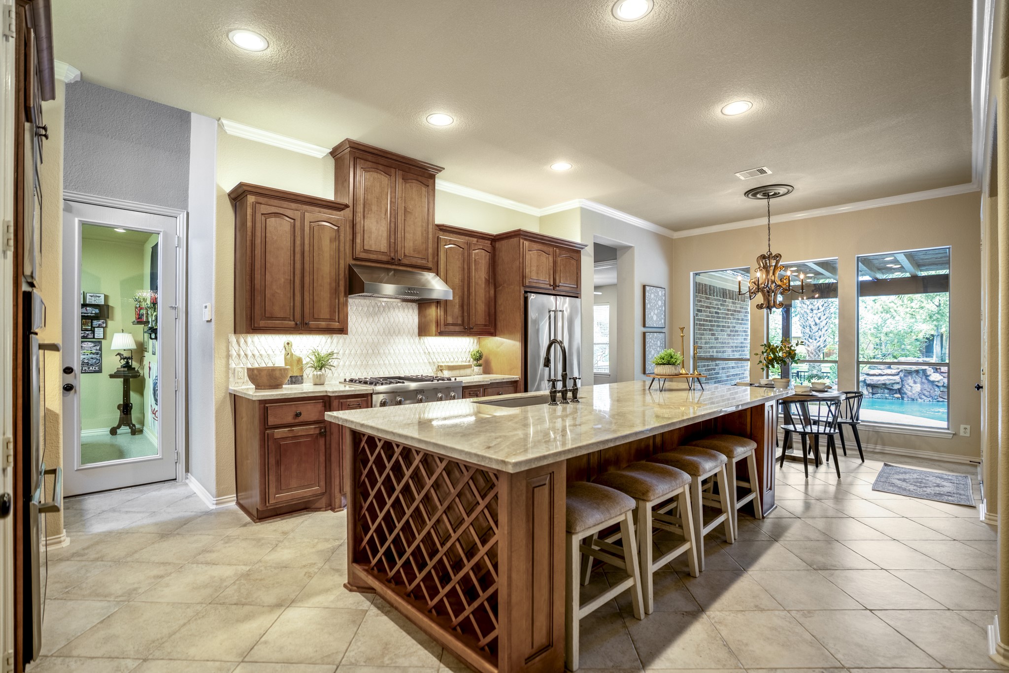 2407 Hendricks Lakes Drive Spring, TX 77388 - Photo 15 of 50 Inside the kitchen, the home’s custom finish really comes together with Taj Mahal quartzite, Benedettini cabinetry, a Dal Tile backsplash, undercabinet lighting, and island seating that keeps the space warm and connected. Built-in wine storage adds a thoughtful detail at the end of the island, while the glass door on the left leads to the separate third garage bay and the breakfast nook ahead opens the view toward the covered patio, pool, and water-front backdrop beyond.
