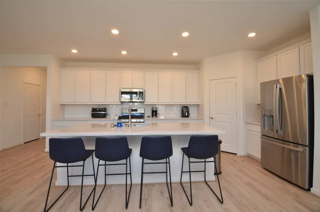 a kitchen with stainless steel appliances a dining table chairs refrigerator sink and cabinets