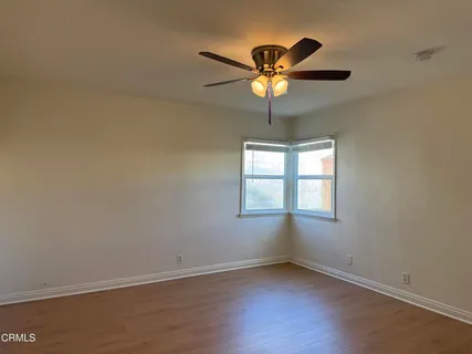 an empty room with wooden floor fan and windows