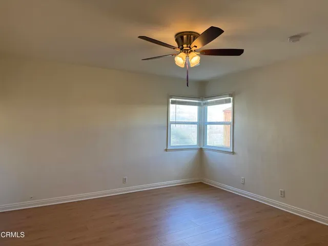 an empty room with wooden floor fan and windows