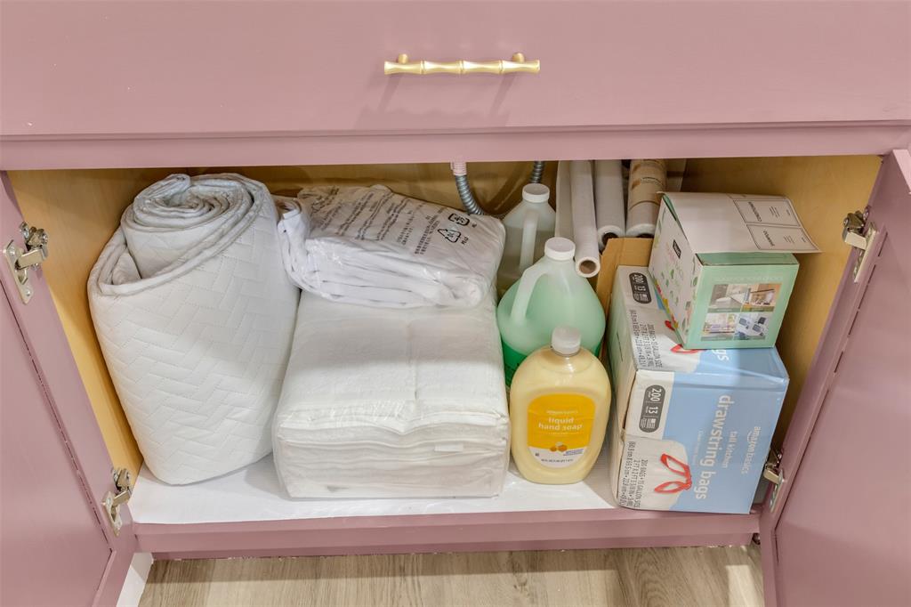 4121 Junius Street, Unit B Dallas, TX 75246 - Photo 31 of 32 Undercabinet storage featuring a pink vanity with a gold-tone bamboo-style handle, white interior shelving, and visible plumbing