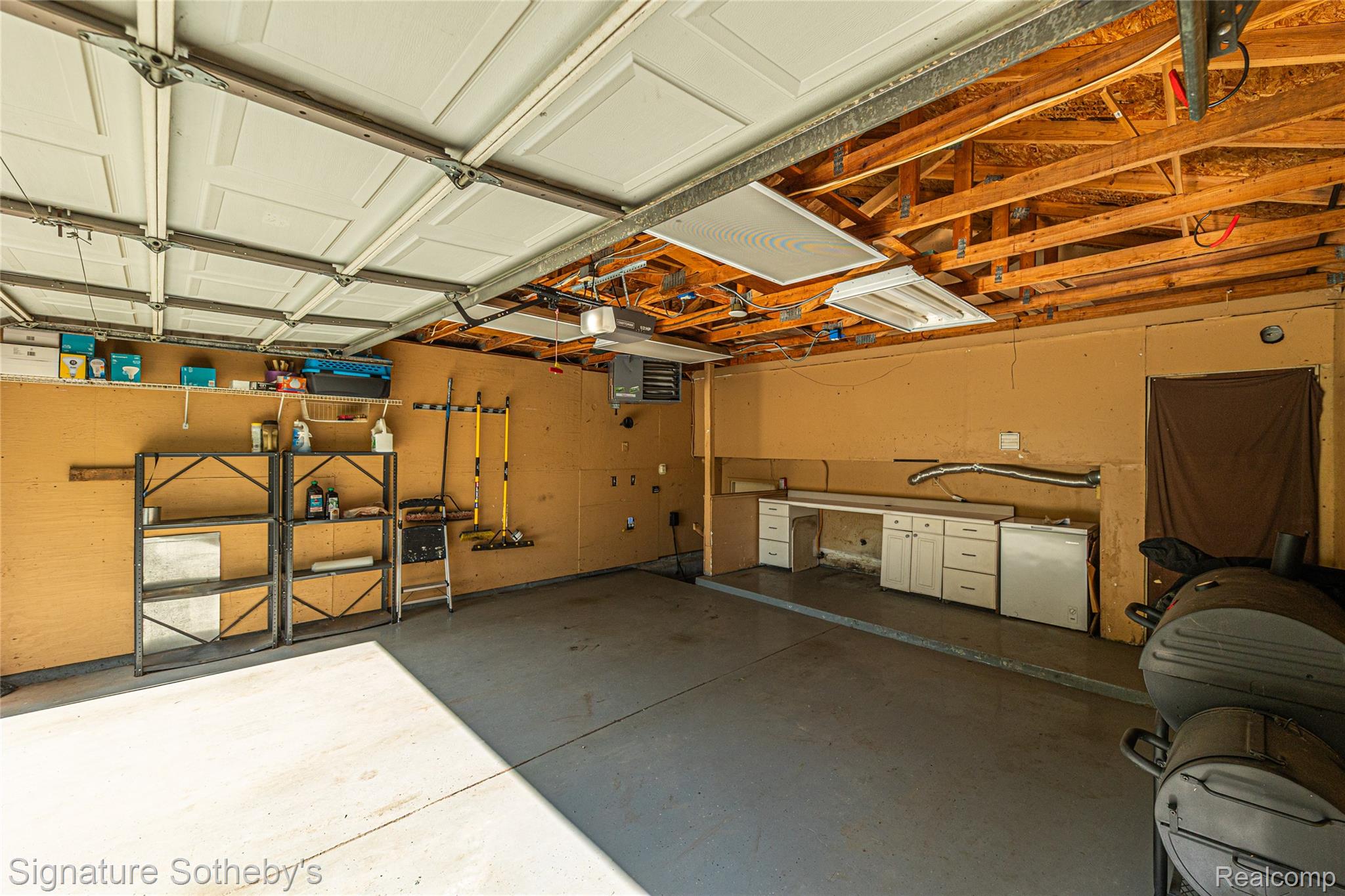 1312 Merry Road Waterford, MI 48328 - Photo 23 of 32 Spacious garage featuring a concrete floor, exposed wood beam ceiling, paneled garage doors, built-in cabinetry, and integrated shelving