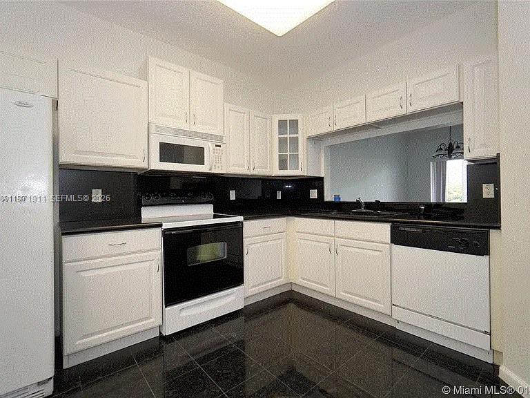8331 Vía Serena, Unit 8331 Boca Raton, FL 33433 - Photo 8 of 8 a kitchen with granite countertop white cabinets and black appliances