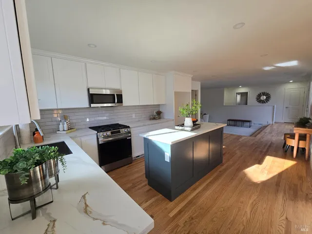 a kitchen with granite countertop a stove a sink a refrigerator and a dining table with wooden floor