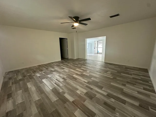 a view of an empty room with wooden floor and a ceiling fan