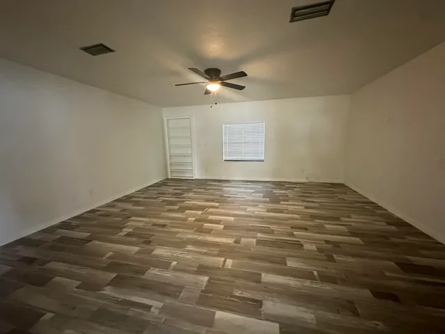 an empty room with kitchen view and a ceiling fan