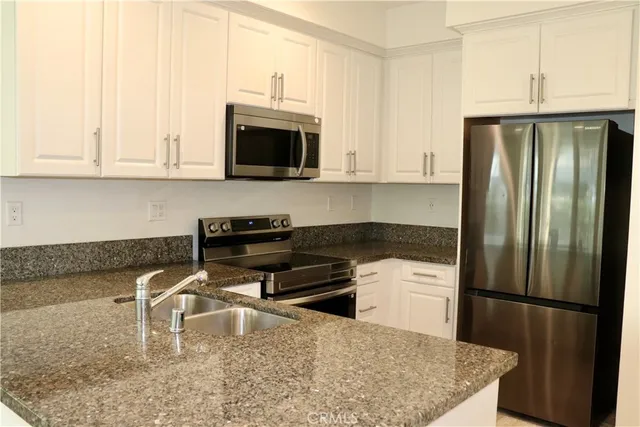 a kitchen with stainless steel appliances granite countertop a refrigerator a stove a sink and white cabinets