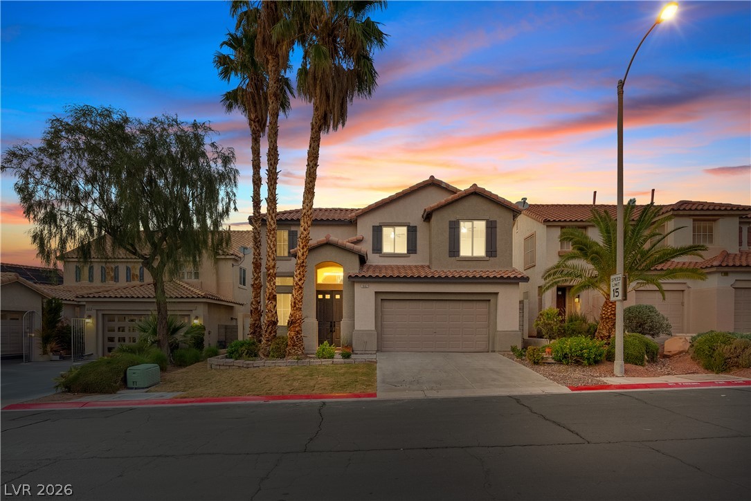 1662 Ravanusa Drive Henderson, NV 89052 - Photo 3 of 74 A charming stucco home with a terracotta-tiled roof, flanked by palm trees under a vivid sunset sky.