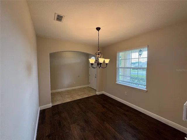 an empty room with wooden floor chandelier and windows