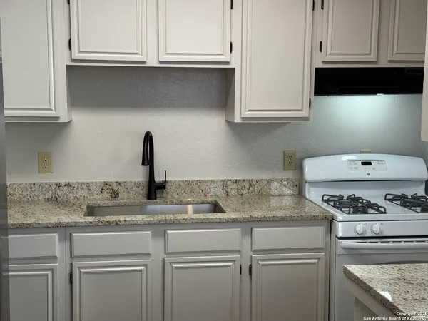 a kitchen with stainless steel appliances granite countertop white cabinets and a stove a sink
