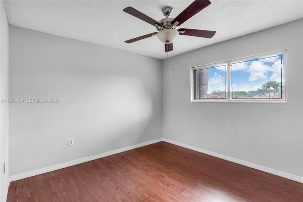 a view of an empty room with wooden floor and a ceiling fan
