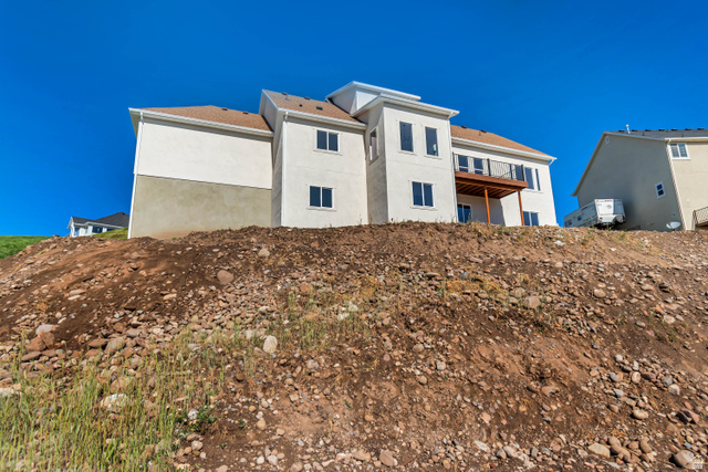1351 Maple Circle Santaquin, UT 84655 - Photo 40 of 42 Contemporary multi-story residence featuring light-colored stucco exterior, multiple window arrangements, a prominent balcony with dark railing, and a contrasting brown shingled roof
