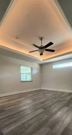 an empty room with wooden floor chandelier fan and windows