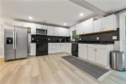 a kitchen with stainless steel appliances granite countertop a refrigerator a sink a stove top oven and white cabinets