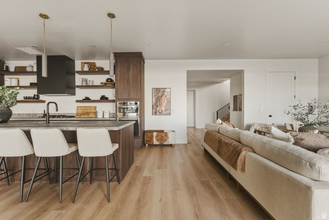 923 North Emery Lane Elk Ridge, UT 84651 - Photo 52 of 101 Open-concept living area featuring wood-finish flooring, a kitchen island with seating, dark wood cabinetry, integrated oven, and a modern range hood