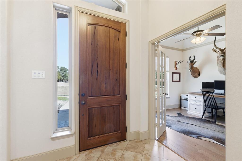 149 Overton Ridge Circle Weatherford, TX 76088 - Photo 3 of 39 Arched wood-panel entry door with sidelights, tile flooring, and french doors opening to a room with wood-finish flooring and a ceiling fan