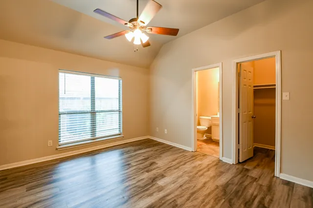 an empty room with wooden floor chandelier fan and windows