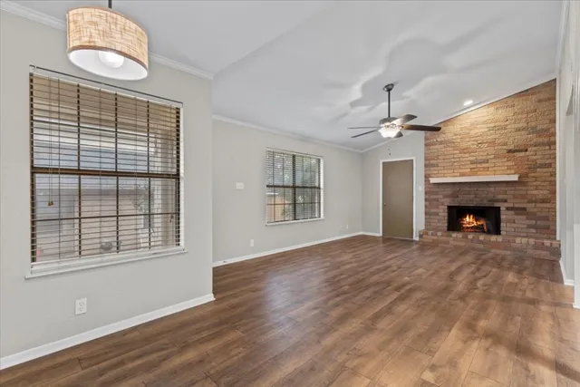 a view of an empty room with wooden floor fireplace and a window