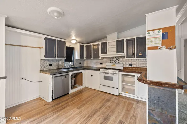 a kitchen with stainless steel appliances granite countertop a refrigerator a sink dishwasher a stove top oven a refrigerator and white cabinets with wooden floor