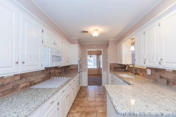 a large white kitchen with granite countertop a sink and white cabinets
