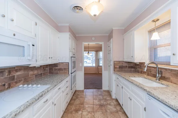 a large kitchen with granite countertop a sink dishwasher a stove and white cabinets