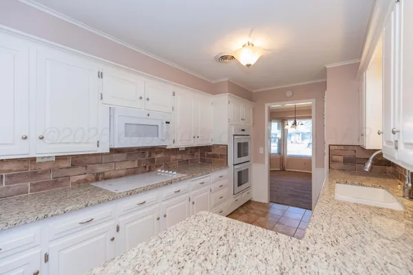 a large kitchen with granite countertop a sink and white cabinets