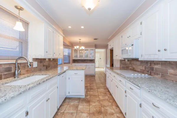 a large kitchen with granite countertop a sink a counter top space appliances and cabinets