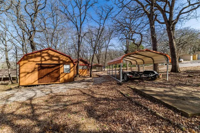 a view of a wooden house with large trees and a wooden fence