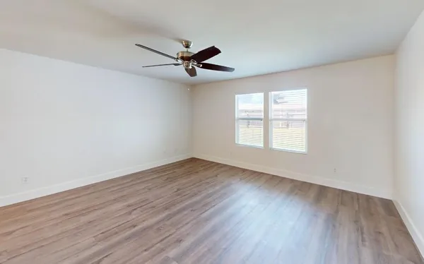 an empty room with wooden floor fan and windows