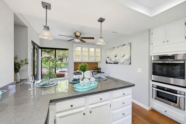 a kitchen with stainless steel appliances kitchen island granite countertop a refrigerator a stove a sink dishwasher and white cabinets with wooden floor