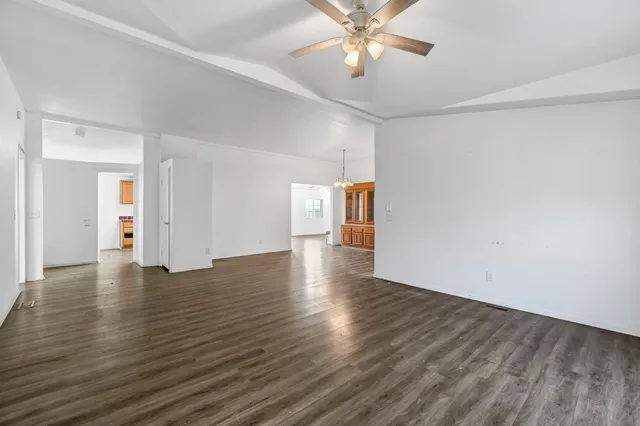 an empty room with wooden floor chandelier fan and windows