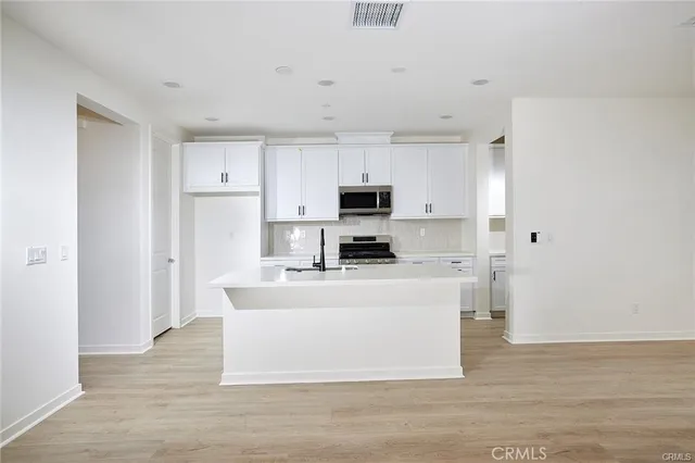 a white kitchen with wooden floor and stainless steel appliances