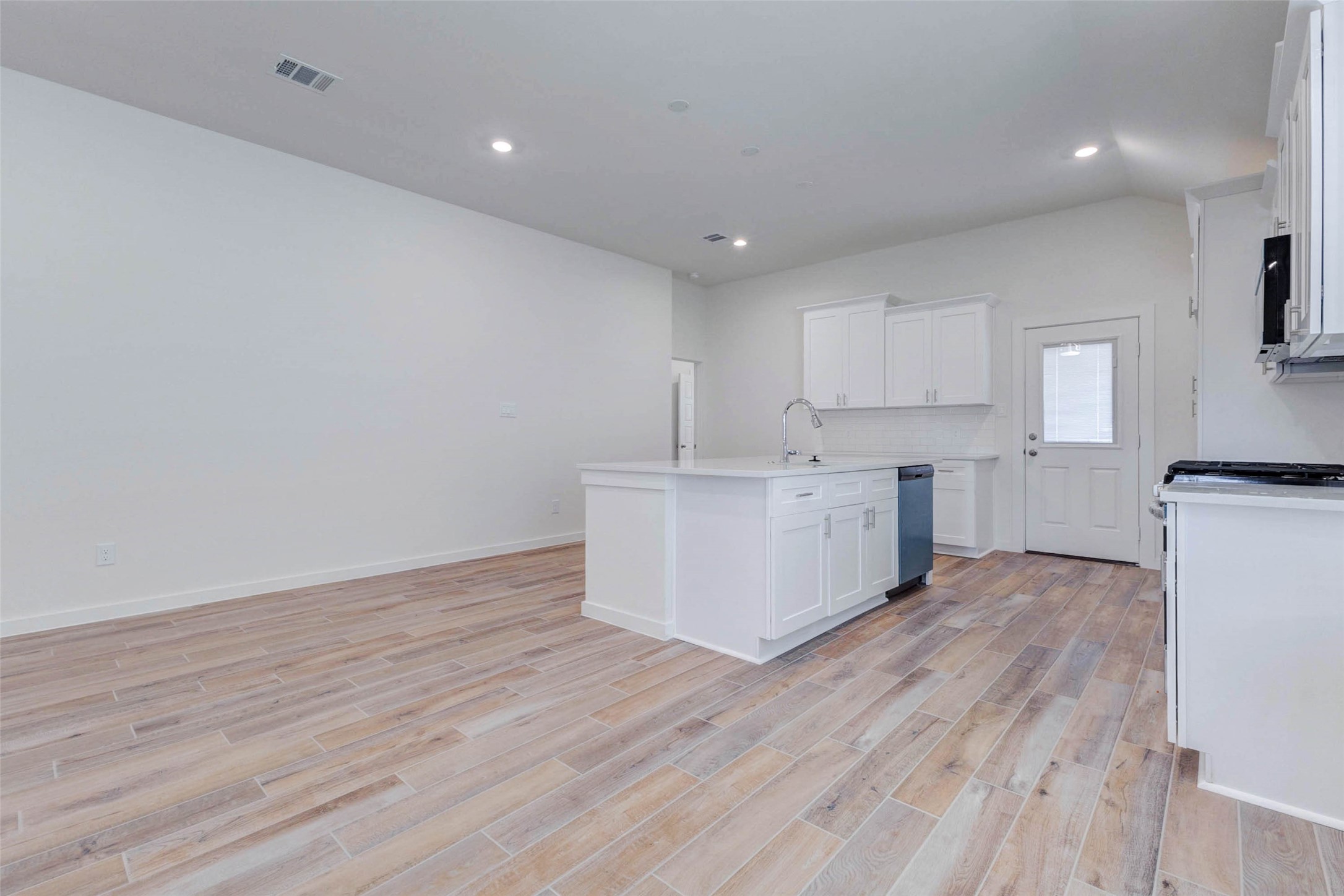 6467 Escondido Drive Rosharon, TX 77583 - Photo 11 of 32 Bright kitchen and dining area featuring wood-look tile flooring, white shaker cabinetry, quartz-style countertops, center island, stainless dishwasher, recessed lighting, and open space for dining. The kitchen flows seamlessly into the main living area for easy entertaining.