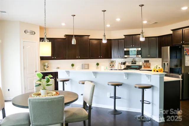 a kitchen with stainless steel appliances kitchen island granite countertop a refrigerator a stove a kitchen island with chairs and wooden floor