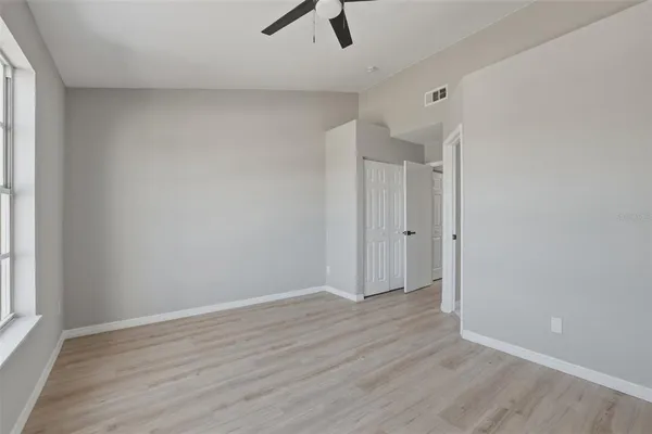 an empty room with wooden floor ceiling fan and windows