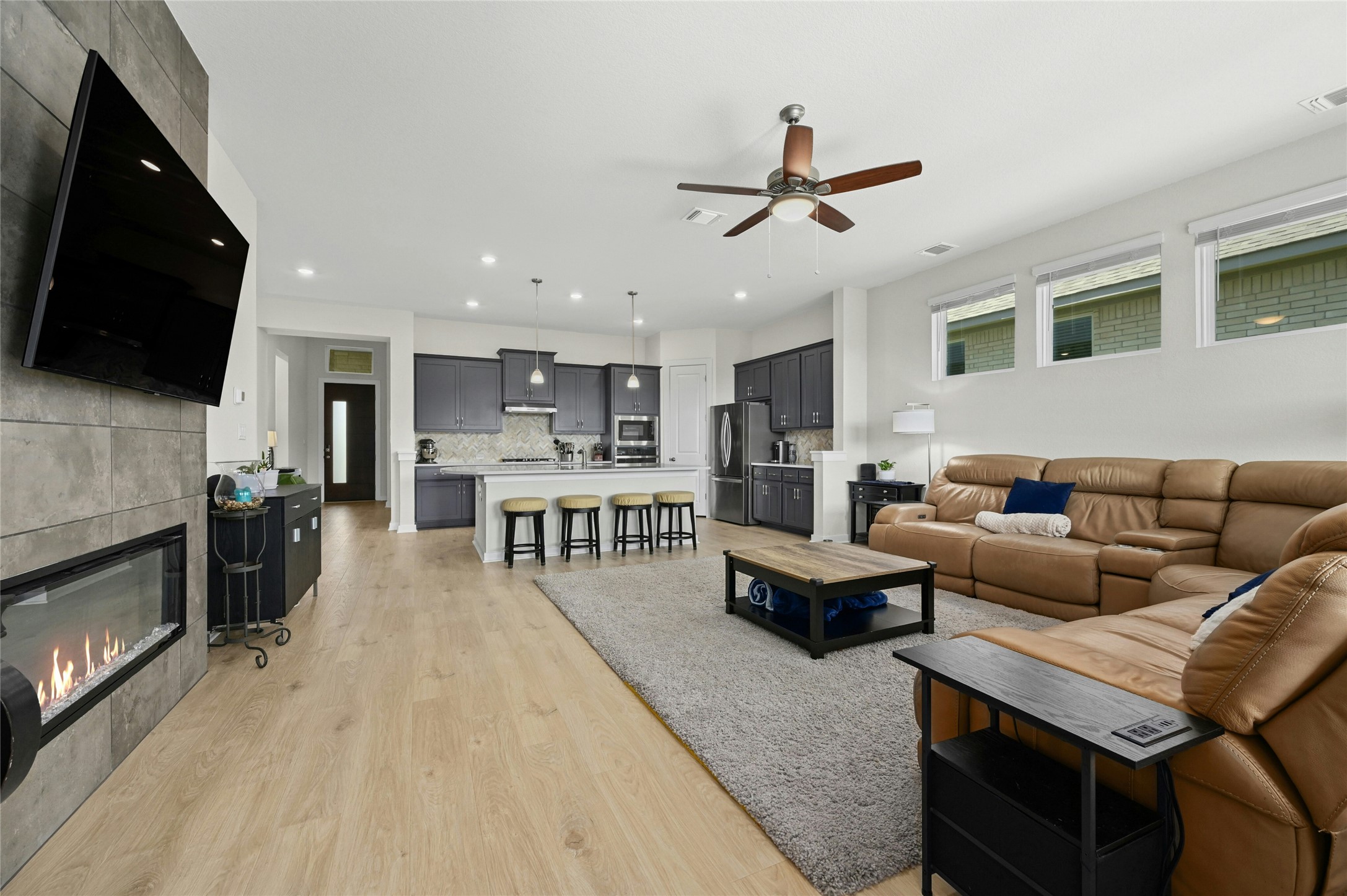 916 Leaning Oak Lane Georgetown, TX 78628 - Photo 11 of 32 Living room featuring a tile fireplace, light wood-style floors, a ceiling fan and a wall of windows allowing for natural lighting