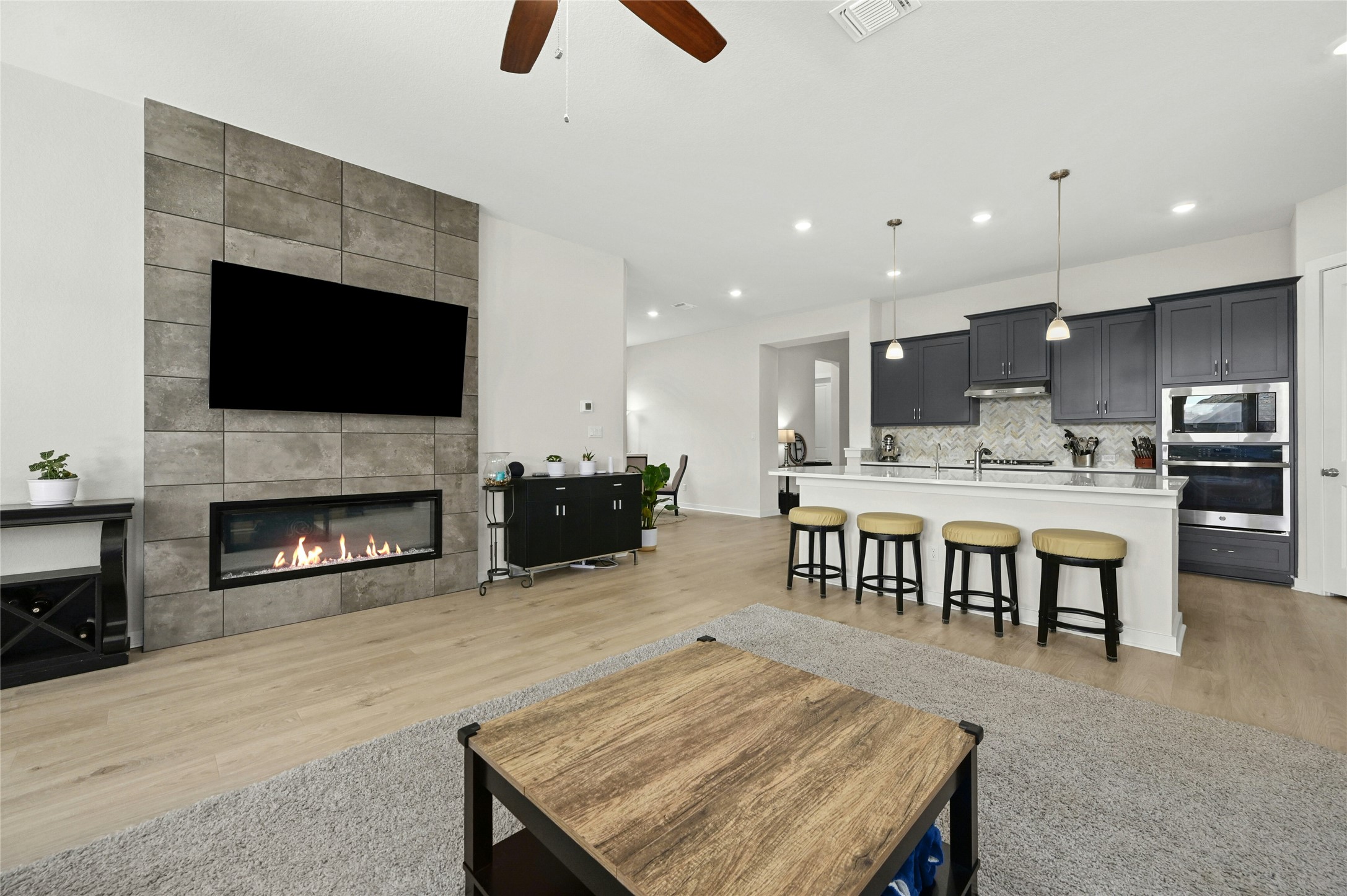 916 Leaning Oak Lane Georgetown, TX 78628 - Photo 12 of 32 Living room featuring a tile fireplace, light wood-style floors, a ceiling fan and a wall of windows allowing for natural lighting