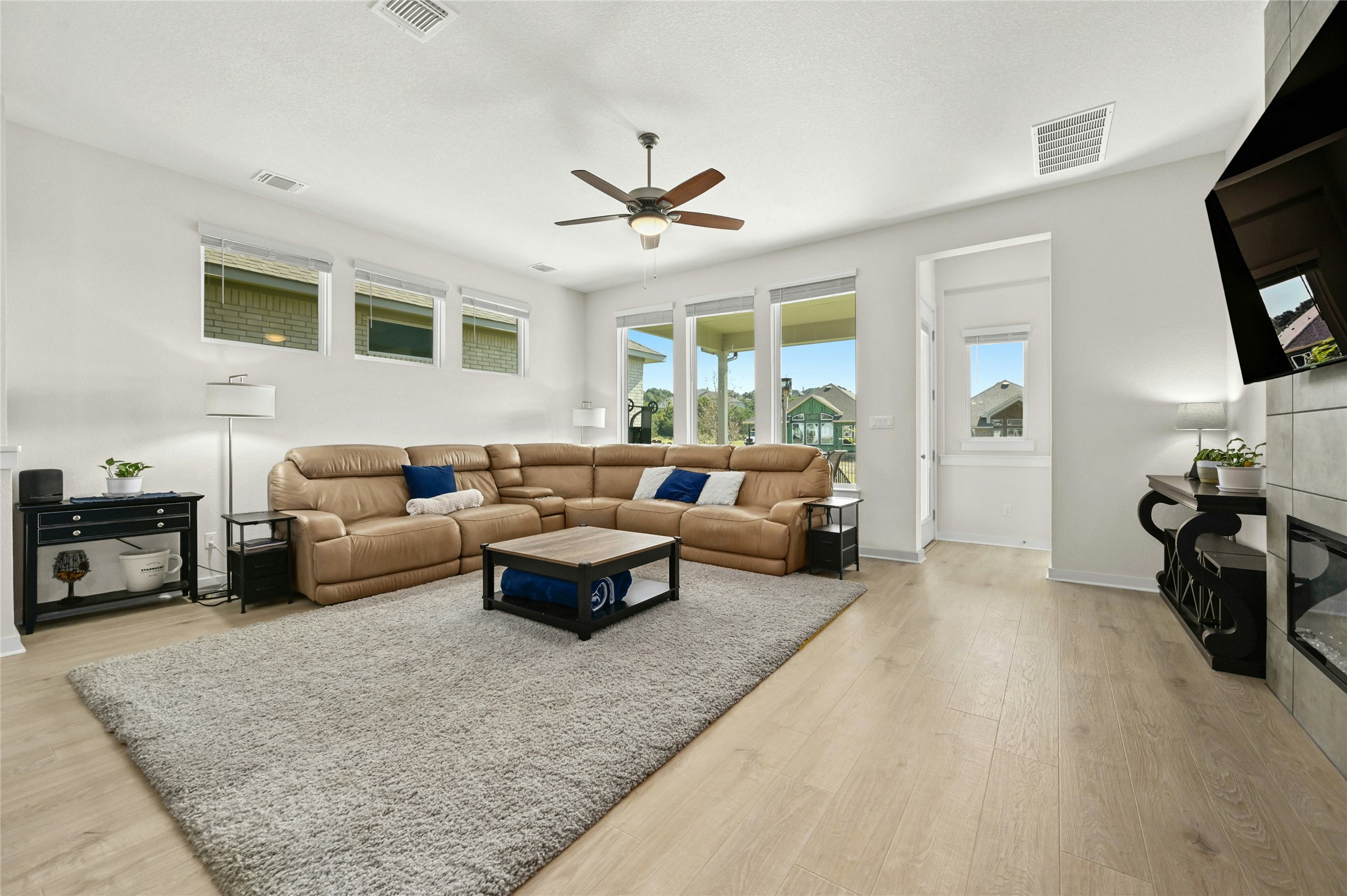 916 Leaning Oak Lane Georgetown, TX 78628 - Photo 10 of 32 Living room featuring a tile fireplace, light wood-style floors, a ceiling fan and a wall of windows allowing for natural lighting