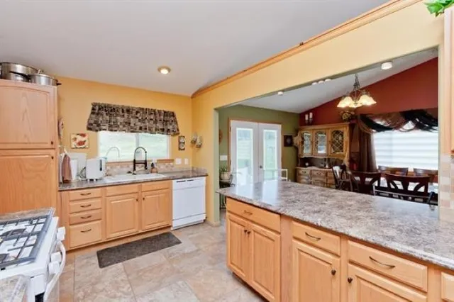 a kitchen with stainless steel appliances granite countertop a stove top oven a sink dishwasher a dining table and chairs with wooden floor