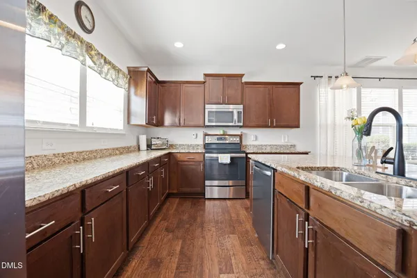 a kitchen with stainless steel appliances granite countertop a sink dishwasher a stove top oven a refrigerator with wooden floors