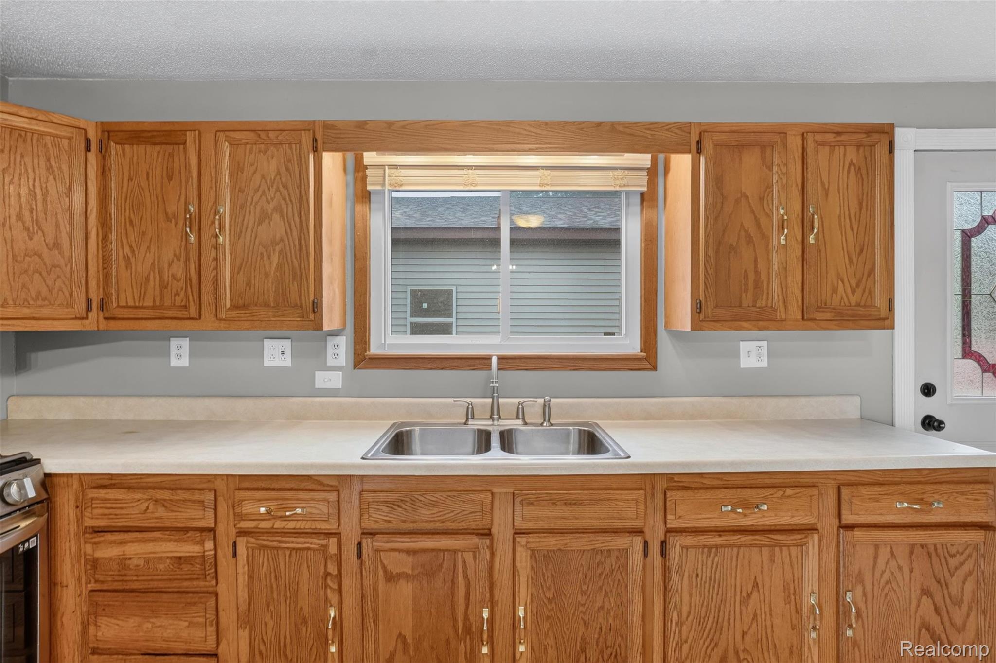 10977 Maple Road Birch Run, MI 48415 - Photo 15 of 49 Light wood cabinetry, laminate countertops, stainless steel double basin sink, chrome faucet, window with wood trim