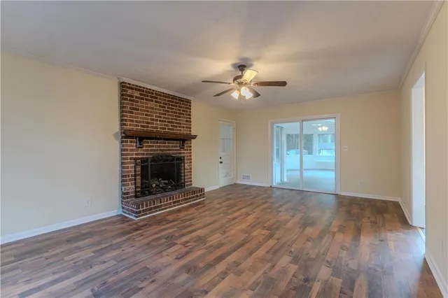 a view of an empty room with wooden floor fireplace and a window
