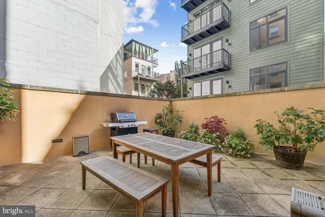 a view of a white house next to a yard with potted plants and large trees